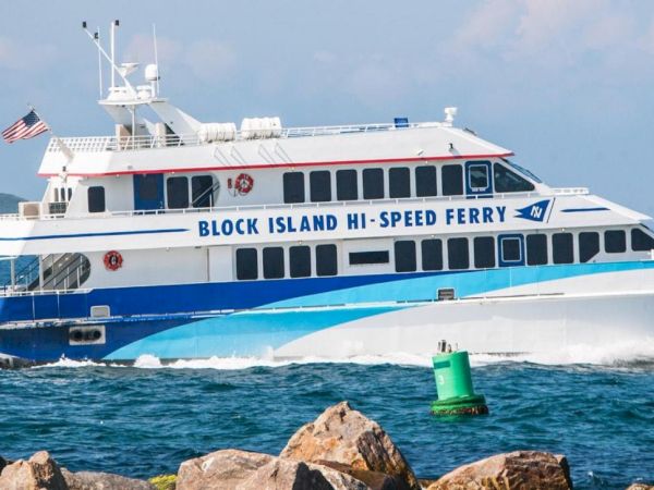 A white ferry named "Islander" with "Block Island Hi-Speed Ferry" written on its side is sailing in the ocean near a rocky shore.