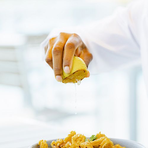 A person squeezes a lemon wedge over a bowl of fried food, possibly calamari, with a dipping sauce on the side.