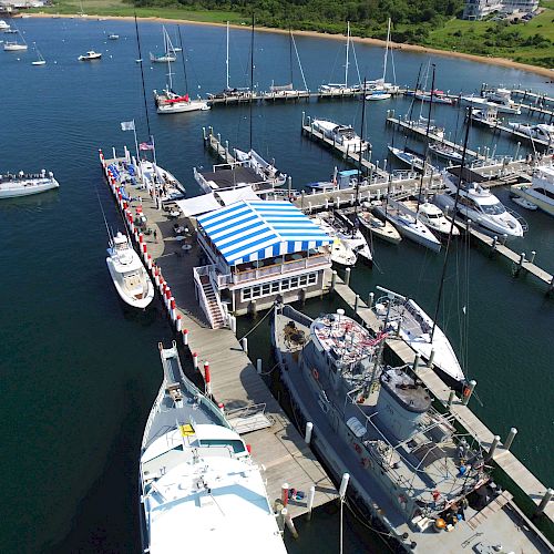 The image shows a marina with several boats docked along piers. There's a small building with a blue and white striped roof in the center of the marina end the sentence.