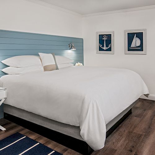 A cozy bedroom with nautical-themed decor, featuring a large bed, blue headboard, and framed pictures of an anchor, sailboat, and ropes on the wall.