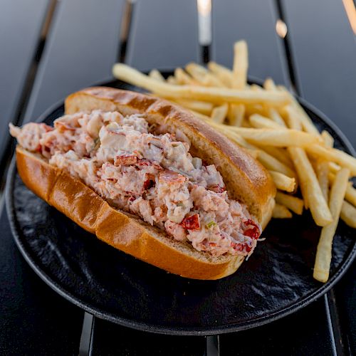 A sandwich filled with a seafood salad, likely lobster or crab, served on a black plate with a side of French fries is shown.