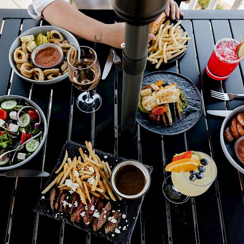 A table with various dishes including salads, fries, shrimp, vegetables, and drinks, with four people dining together.