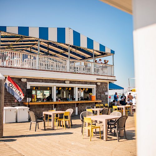 A two-story beachside cafe with a striped awning, outdoor tables, and an 