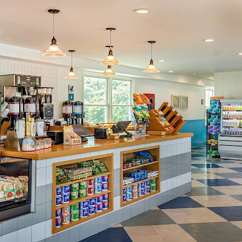 This image shows the interior of a modern café or convenience store with a counter, food items, and a large refrigerator with drinks in the background.