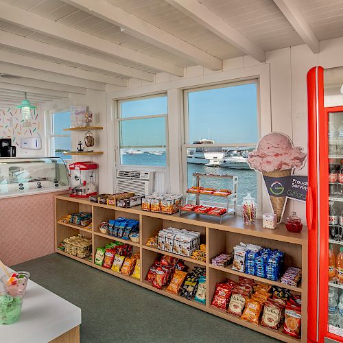 This image shows an ice cream shop interior with a display case, shelves of snacks, candy jars, and a refrigerator filled with drinks.