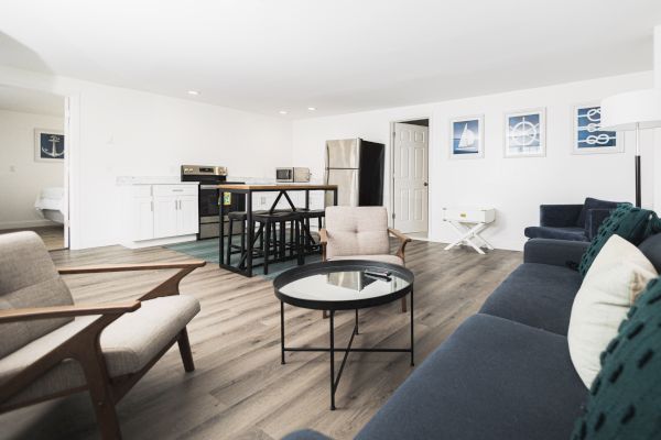 A modern living room features a navy couch, beige chairs, and a black round coffee table, with a kitchen area in the background.