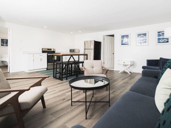 A modern living room features a navy couch, beige chairs, and a black round coffee table, with a kitchen area in the background.