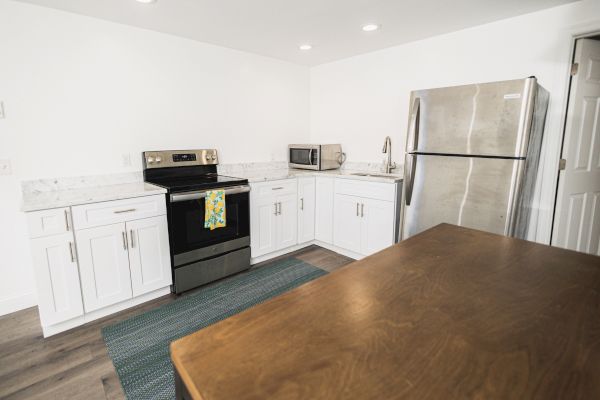 A modern kitchen featuring white cabinets, a stainless steel refrigerator, a stove, a microwave, and a wooden countertop.