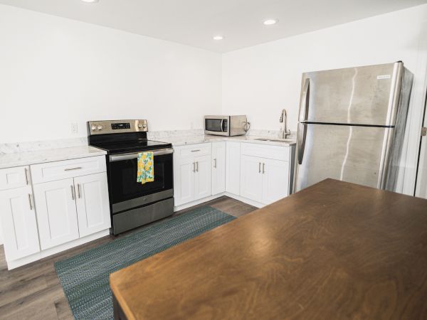 A modern kitchen featuring white cabinets, a stainless steel refrigerator, a stove, a microwave, and a wooden countertop.
