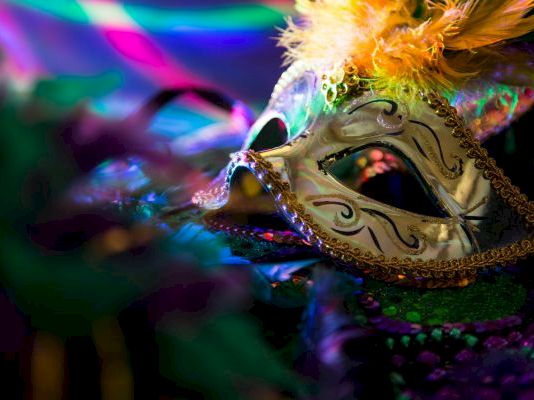 A ornate masquerade mask with gold filigree and feathers, set against vibrant, neon-lit colors and shimmering beads, mysterious elegance.