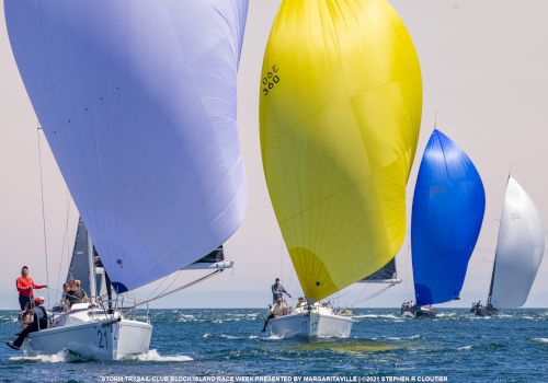Several sailboats with colorful sails compete on open water under a clear sky.