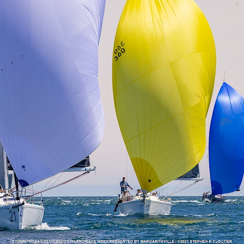 Several sailboats with colorful sails compete on open water under a clear sky.