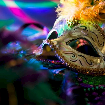 A ornate masquerade mask with gold filigree, feather accents, and colorful lighting, suggesting a festive carnival or masquerade theme.