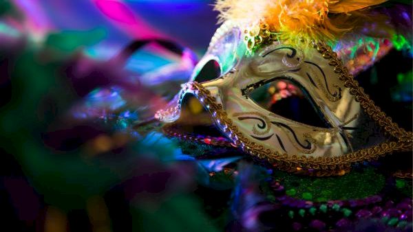 A ornate masquerade mask with gold filigree, feather accents, and colorful lighting, suggesting a festive carnival or masquerade theme.