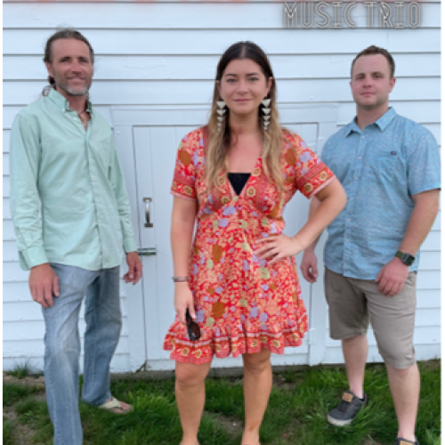 Three individuals stand in front of a white wall with the text 