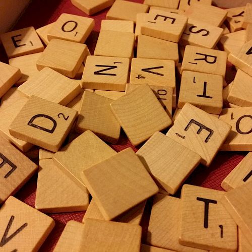 The image shows a pile of wooden Scrabble letter tiles scattered on a surface, some face-up and some face-down.