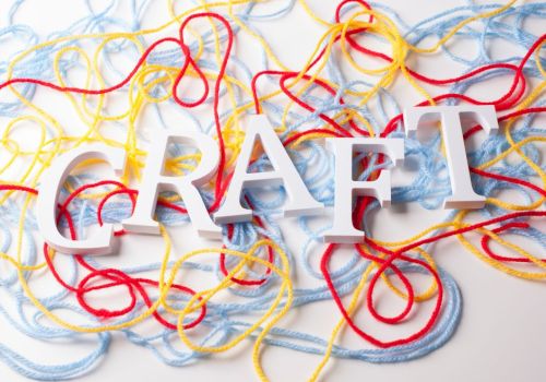 Three-dimensional white letters spelling "CRAFT" sit atop a background of tangled red, yellow, and blue yarn.