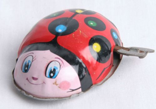 A toy ladybug with a red shell, black spots, and a smiling face, likely wind-up with the key visible on the side, on a white background.