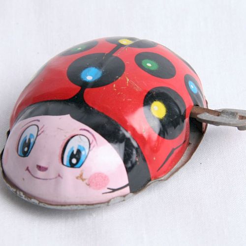 A toy ladybug with a red shell, black spots, and a smiling face, likely wind-up with the key visible on the side, on a white background.