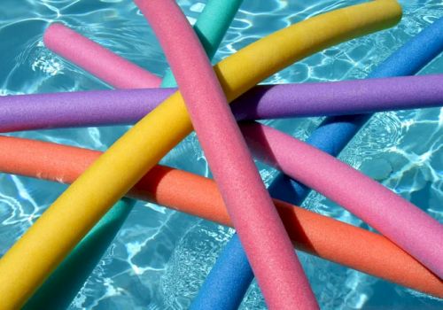 The image shows colorful pool noodles floating in a swimming pool with clear blue water.
