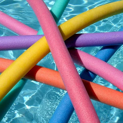 The image shows colorful pool noodles floating in a swimming pool with clear blue water.