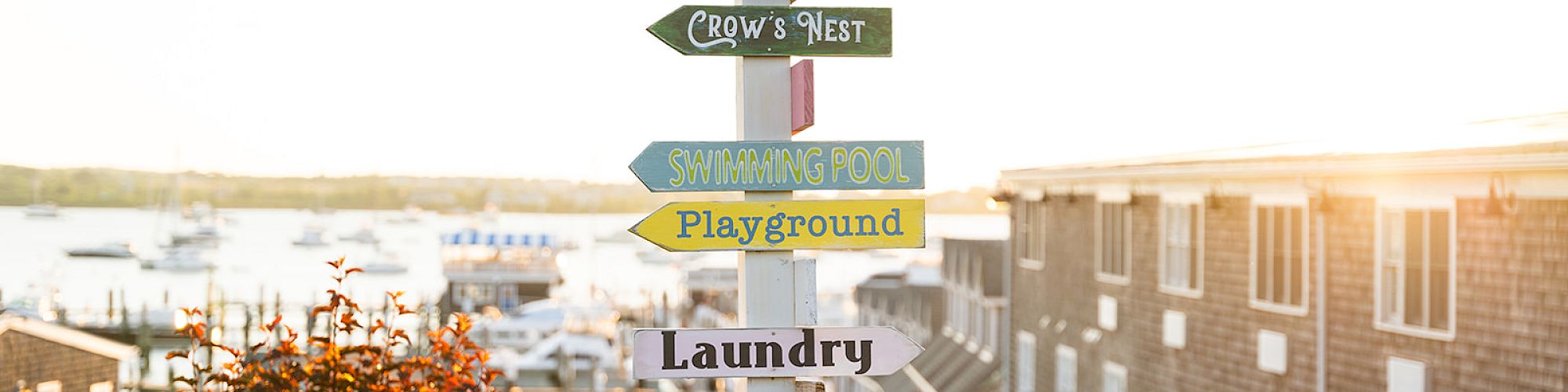 A signpost with multiple colorful directional signs points to various locations like parking, swimming pool, playground, laundry, and event tent.