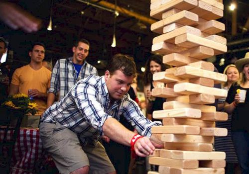 People are gathered at an indoor event, watching a man play a giant Jenga game.