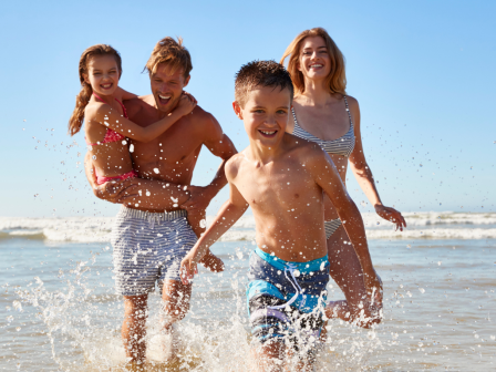 A family of four is having fun on a sunny beach, playing in the water and smiling while enjoying their time together.