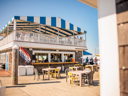 An outdoor café with a blue-and-white striped roof, featuring tables, chairs, and an 