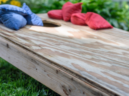 This image shows a wooden cornhole board on grass with red and blue bean bags placed on top of it.