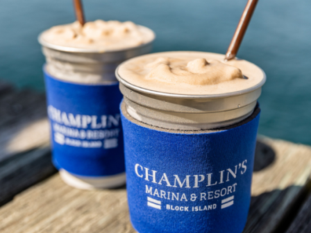 Two frozen drinks in mason jars with straws, in blue koozies labeled 