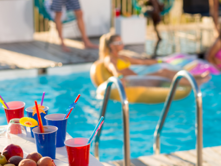 People enjoying a pool party with colorful drinks by the poolside while some relax on inflatable floaties in the water, soaking up the sun.