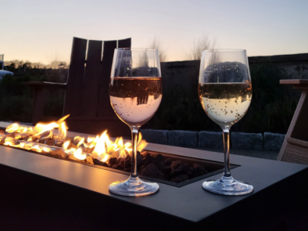 Two glasses of white wine on a table with a fire pit, and an outdoor seating area at sunset providing a cozy atmosphere.