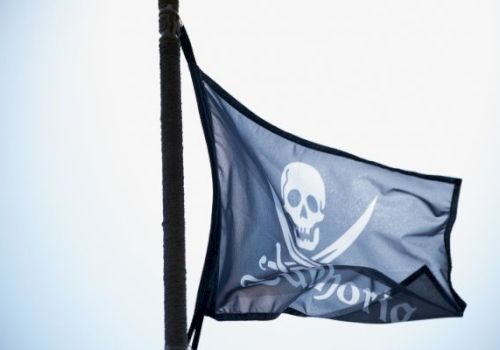 Pirate flag with a skull and crossed swords waving on a pole outdoors.