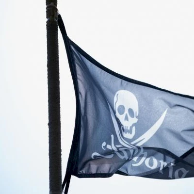 Pirate flag with a skull and crossed swords waving on a pole outdoors.