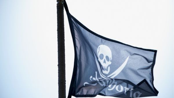 Pirate flag with a skull and crossed swords waving on a pole outdoors.