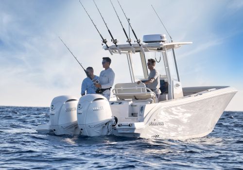 Three men on a sleek white fishing boat with multiple rods, moving through blue ocean under a clear sky.