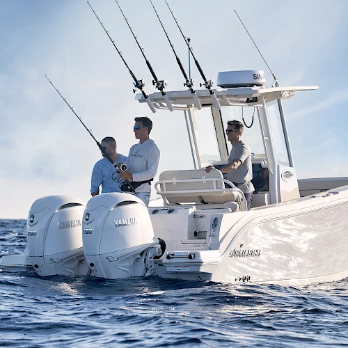 Three men on a sleek white fishing boat with multiple rods, moving through blue ocean under a clear sky.