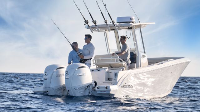 Three men on a sleek white fishing boat with multiple rods, moving through blue ocean under a clear sky.