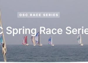 Sailboats compete in the OSC Spring Race Series on the open sea, with colorful sails against a clear sky in the background.