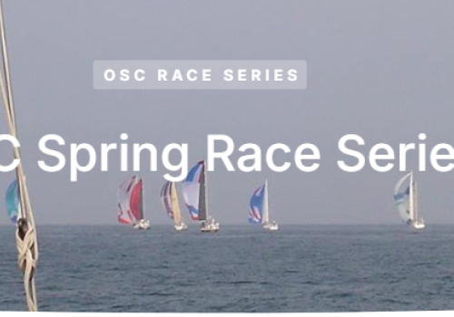 Sailboats compete in the OSC Spring Race Series on the open sea, with colorful sails against a clear sky in the background.