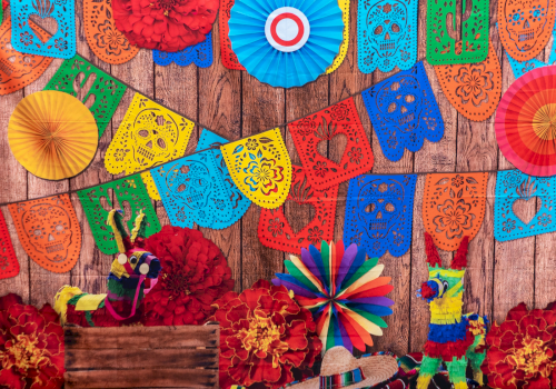 Colorful papel picado banners, paper rosettes, flowers, and pi&ntilde;atas adorn a rustic wooden backdrop for a festive Fiesta mood.