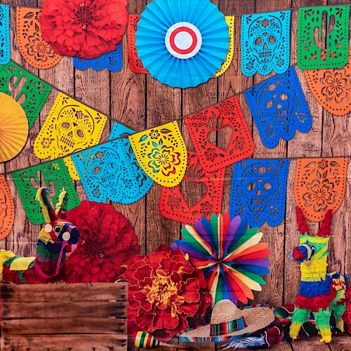 Colorful papel picado banners, paper rosettes, flowers, and pi&ntilde;atas adorn a rustic wooden backdrop for a festive Fiesta mood.