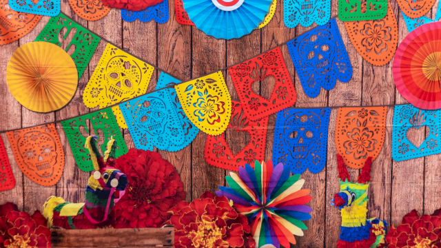 Colorful papel picado banners, paper rosettes, flowers, and pi&ntilde;atas adorn a rustic wooden backdrop for a festive Fiesta mood.