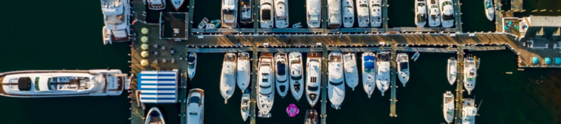 An aerial view of a marina with numerous boats docked in rows alongside piers in deep blue water.