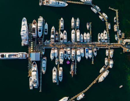 An aerial view of a marina with numerous boats docked in rows alongside piers in deep blue water.