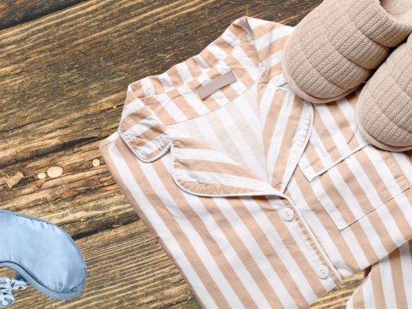 A striped beige and white button-up shirt laid on a wooden floor, with a pair of slippers nearby and a blue sneaker in view.