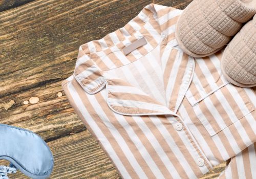A beige and white striped shirt laid on a wooden floor with slippers nearby, suggesting a casual outfit on the go.