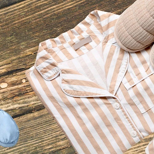A beige and white striped shirt laid on a wooden floor with slippers nearby, suggesting a casual outfit on the go.