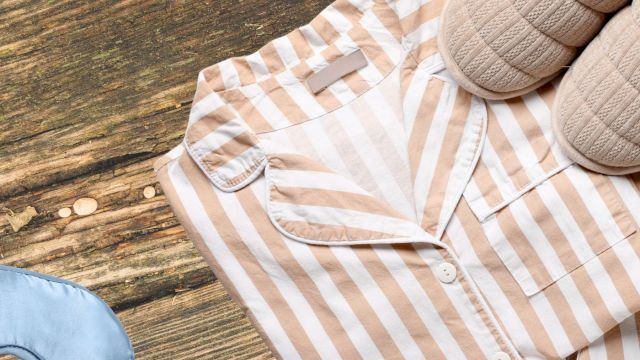 A beige and white striped shirt laid on a wooden floor with slippers nearby, suggesting a casual outfit on the go.